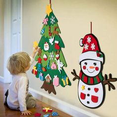 a little boy playing with christmas decorations on the wall next to a snowman and tree