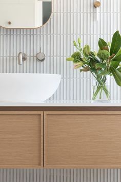 a white sink sitting under a bathroom mirror next to a wooden cabinet with a plant in it