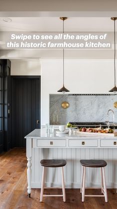 a kitchen island with three stools in front of it and two lights hanging from the ceiling