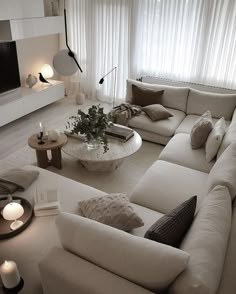 a living room filled with lots of white furniture and candles in front of a large window