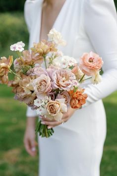 a woman in a white dress holding a bouquet of pink and orange flowers on her wedding day