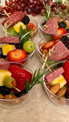 four plastic bowls filled with different types of fruit and nuts on top of a table