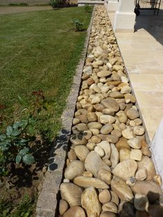 there is a long row of rocks on the side of this house that has grass in front of it