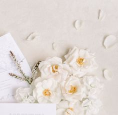 the wedding stationery is laid out with white flowers and greenery on it's side