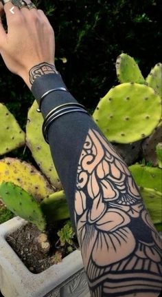 a person's arm with tattoos on it next to some cactuses and plants