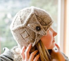 a woman wearing a knitted hat while talking on her cell phone in front of a window