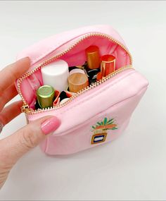 a hand holding a pink purse filled with cosmetics