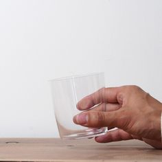 a hand holding a glass on top of a wooden table next to a white wall