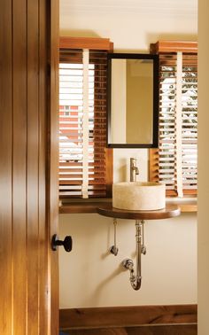 a bathroom sink sitting under a mirror next to a wooden window sill with shutters