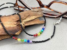 Tiny black seed beads necklace with chakra colors gemstones. Elegant and bohemian eye glasses necklace chain in black tones with rainbow touches in the seven colors of the chakras. The necklace is made with Preciosa Czech seed beads and tiny Amethyst, Turquoise, Jade, Agate, Citrine, Carnelian and Ruby gemstones. Paired with tiny silver plated crystal seed beads, this handmade eyeglass chain will definitely create a unique look. This eyeglass lanyard is made on strong quality beading wire with s Black Glass Beaded Necklaces With Colorful Beads, Black Glass Beaded Necklaces With Beaded Chain, Black Glass Beaded Necklace With Colorful Beads, Black Glass Beaded Necklace With Beaded Chain, Black Glass Beaded Necklace, Black Spiritual Necklace For Beach, Black Bohemian Glass Jewelry, Bohemian Black Glass Jewelry, Black Glass Bohemian Jewelry