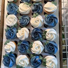 cupcakes with blue and white frosting are arranged in a square box on a table