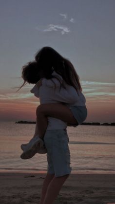 a woman holding a child on the beach at sunset