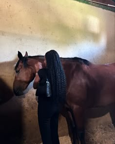 a woman standing next to a brown horse in a stable with her head against the wall