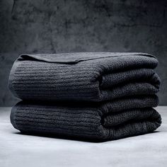 three folded black towels stacked on top of each other in front of a gray wall