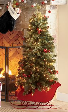 a small christmas tree in a red sleigh next to a fireplace with stockings on it