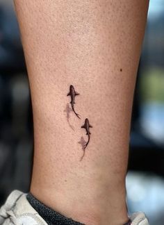 a small tattoo on the ankle of a woman's leg, with two birds flying above