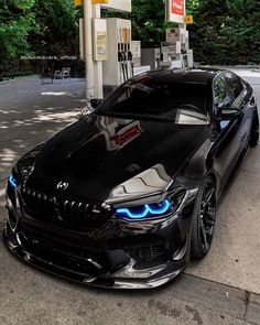 a black car parked in front of a gas station with blue lights on it's hood