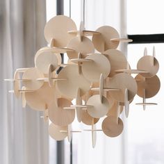 a chandelier made out of wooden discs hanging from the ceiling in front of a window