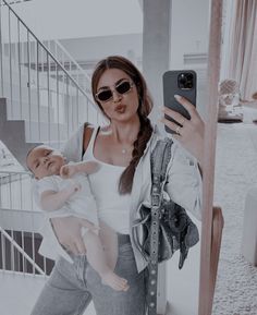 a woman taking a selfie while holding a baby in her arms and wearing sunglasses