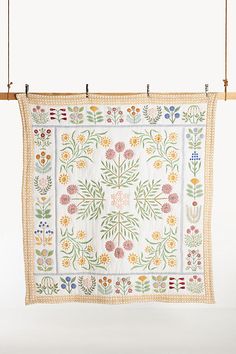 an embroidered wall hanging with flowers and leaves on the front, along with two wooden pegs