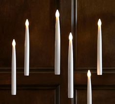 several white candles are lined up in front of a wooden door with the lights turned on