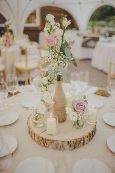 there is a vase with flowers and candles on top of a wooden slice in the middle of a table