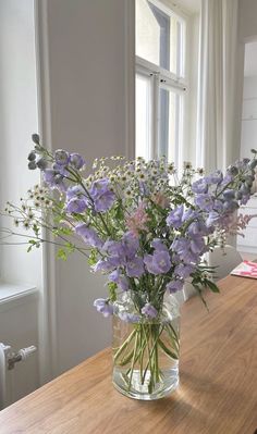 a vase filled with purple flowers sitting on top of a wooden table next to a window