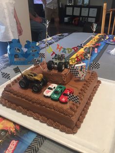 a birthday cake with cars on it sitting on a table in front of some people