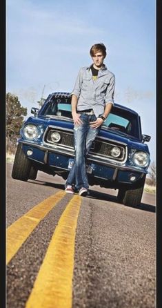 a young man sitting on the hood of a blue car with his hands in his pockets