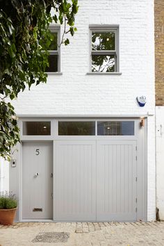 a white house with two windows and a door on the outside, next to a potted tree