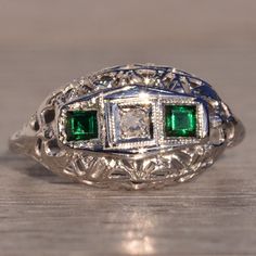 The 132nd Avenue: Antique Filigree Diamond And Emerald Ring In White Gold. The Ring Centers On An Old Cut Natural Diamond Inside A Square Box Finished With Very Fine Milgrain. On Either Side Of The Center Is A Carre Cut Lab-Grown Emerald With A Deep Very Slightly Bluish-Green Color In A Finely Milgrained Bezel. An Intricate Filigree Pattern Exists Throughout The Top Of The Ring Into The Through-Finger View And Shank. The Ring Is Crafted In 14 Karat White Gold And Is Currently A Finger Size 3.25 Yet Can Be Adjusted To Any Finger Size For An Additional Charge On Request. Antique Emerald Engagement Ring, Diamond And Emerald Ring, Antique Filigree, Filigree Pattern, Bluish Green, Emerald Engagement Ring, Emerald Ring, Vintage Diamond, Womens Jewelry Rings