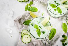 two glasses filled with cucumber, mint and lemonade on top of a towel