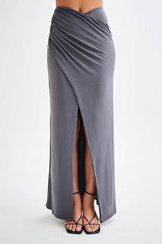 For a summer escapade.The BRONWYN Slinky Ruched Maxi Skirt With Split is a sophisticated and stylish piece designed to make a statement. Featuring a mid-rise fit and a flattering V front, this skirt enhances your natural curves. The centre front split adds a touch of allure, while the ruching at the side seams provides a chic, textured look. Made with stretch fabrication, it ensures comfort and ease of movement. For a complete and stunning outfit, pair this skirt with the Bronwyn Slinky Halter C Elegant Ruched Skirt In Solid Color, Elegant Ruched Solid Color Skirt, Elegant Solid Ruched Skirt, Elegant Ruched Maxi Skirt For Summer, Date Night Ruched Stretch Skirt, Chic Draped Fitted Maxi Skirt, Stretch Draped Bottoms For Night Out, Ruched Draped Maxi Skirt For Party, Chic Fitted Ruched Maxi Skirt