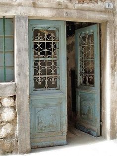 an old stone building with two blue doors and one has a wrought iron screen on the door