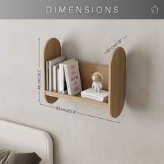 a wooden shelf with books on it next to a white wall and a bed in the background