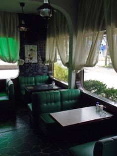 the inside of a restaurant with green couches and tables in front of large windows