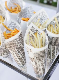 french fries in paper cups are sitting on a glass tray with newspaper wrappers around them