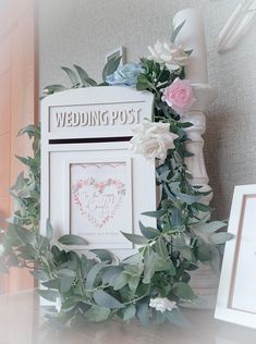 a wedding post box with flowers and greenery on it next to a framed photo