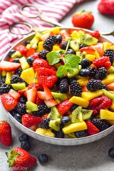 a bowl filled with fruit salad next to sliced strawberries