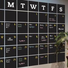 a large black and white calendar with numbers on the wall next to a potted plant