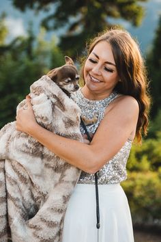 a woman holding a cat in her arms and smiling at the camera while wearing a white dress