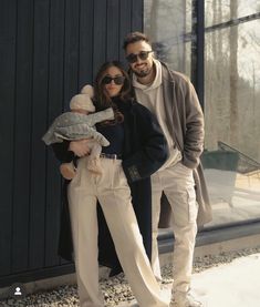 a man and woman standing next to each other in front of a building holding a baby