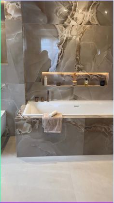 a bath tub sitting next to a white sink under a mirror in a bathroom with marble walls