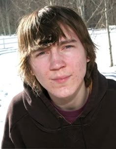 a young man standing in the snow wearing a hoodie and looking at the camera