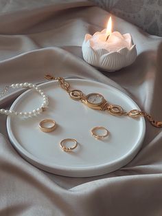 a white plate topped with gold jewelry and a candle on top of a cloth covered table