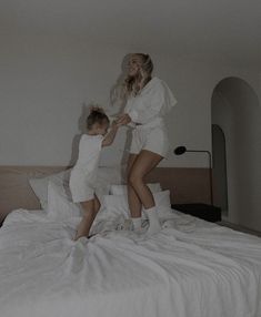 a woman in white is playing with a child on top of a bed and another person standing next to her