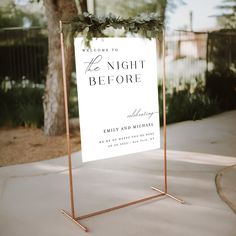 a sign that is sitting on the sidewalk near a tree and bushes with greenery around it