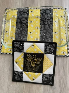 a yellow and black patchwork tray with a bee on it, sitting next to a glass dish