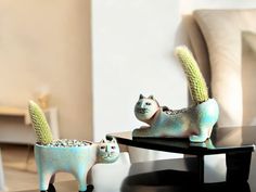 two small ceramic cats sitting next to each other on top of a black coffee table