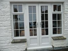 a white double door with two windows in front of a brick building and stone steps